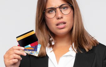 young woman with a credit card feeling puzzled and confused, with a dumb, stunned expression looking at something unexpected