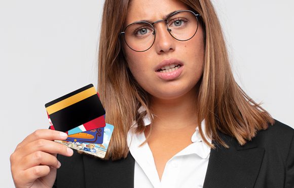 young woman with a credit card feeling puzzled and confused, with a dumb, stunned expression looking at something unexpected